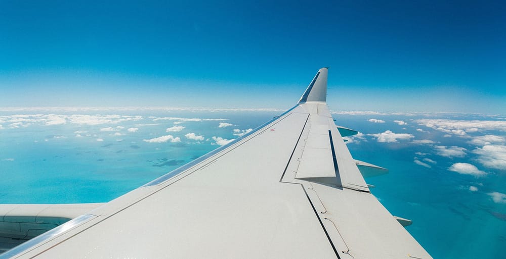 Airfare inflationary spike aircraft wing seen from cabin over clouds